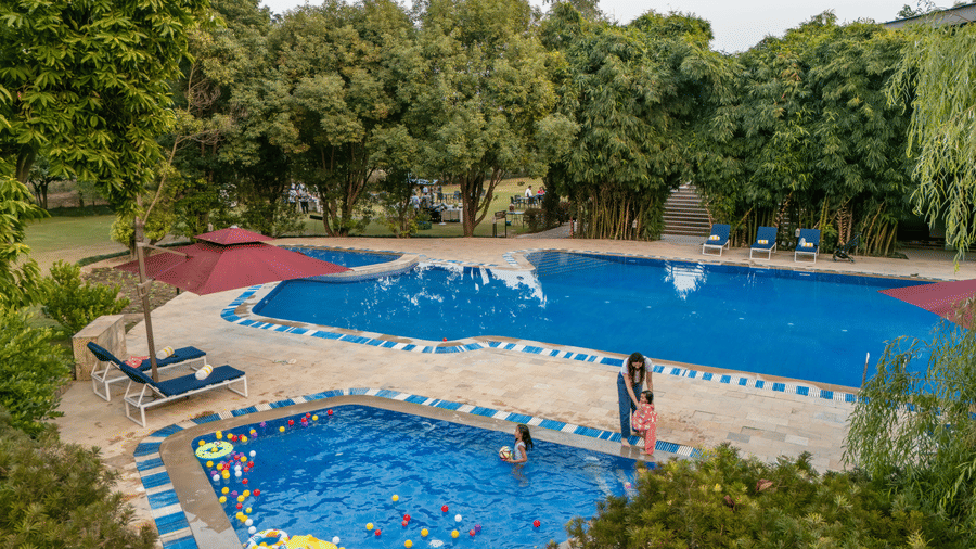 swimming pool with surrounding greenery and buildings in the background at The Golden Tusk, Jim Corbett