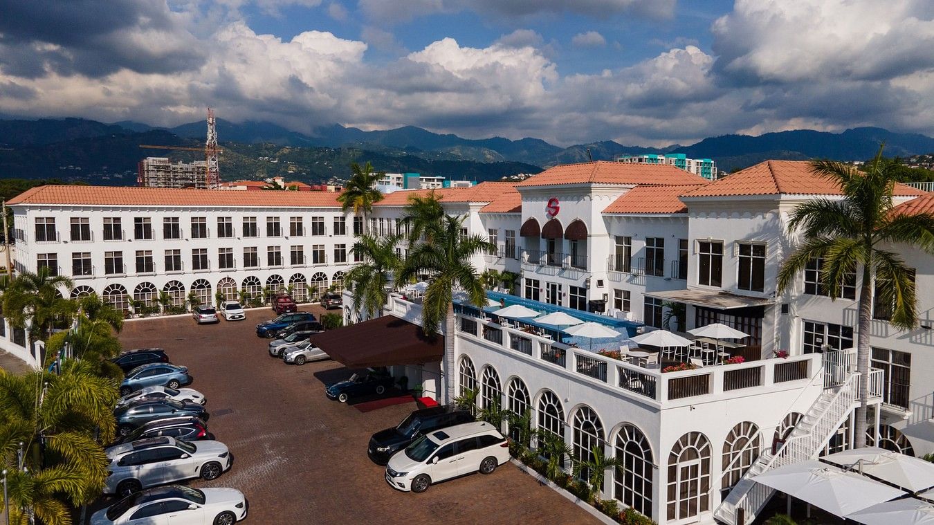 An aerial image of our hotel in Kingston, embraced by lush green palm trees and a spacious parking area - S Hotel Kingston, Jamaica