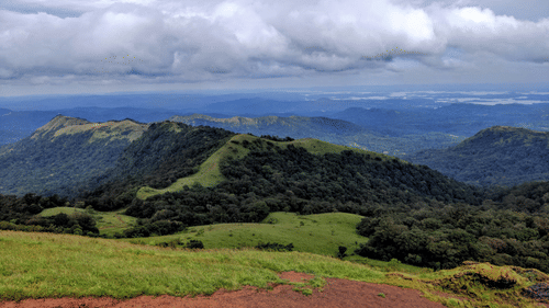 Scenic view of Baba Budangiri hills with lush green slopes, misty valleys, and dramatic clouds over the Western Ghats.