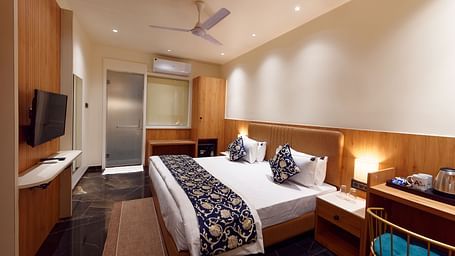 Image of deluxe room with a bed with table and chair on the side of the table and a fan on te ceiling at Ankit Hotel, Jabalpur