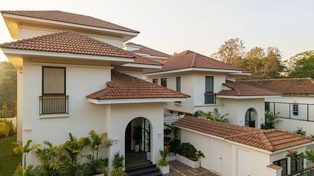 A top view of the property where the architecture is prominent along with the gate, railings, plants around the property with an impression of the sunlight and big trees visible i the background. - BluSalzz Villas - Alocassia, Anjuna