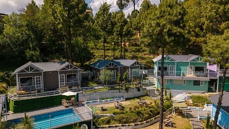 Aerial view of modern cabins and a swimming pool nestled in a wooded hillside - DLS Nature Trinket Resort, Dalhousie.