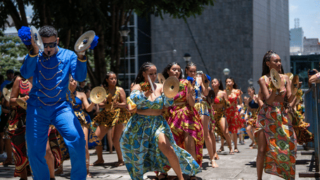 Group of dancers in colourful patterned outfits performing during a lively outdoor street parade in the city.