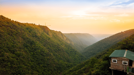 Panoramic view of Mawkdok Dympep Valley in Meghalaya, featuring lush green hills, a deep forested gorge, and a golden sunset illuminating the landscape.