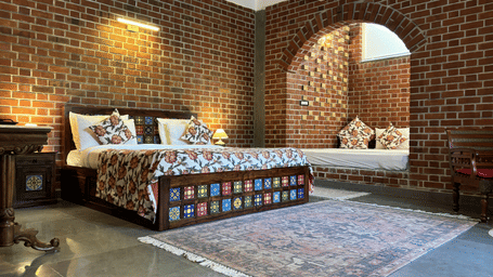 Bedroom with double bed, patterned bedding, and arched brick window at Tisya Farms, Gurgaon.
