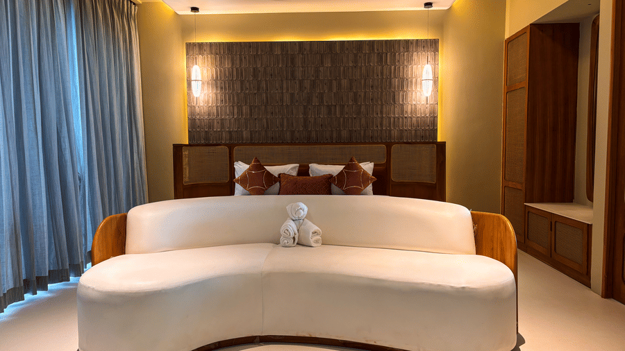 A wide white sofa with a small white towel animal sits in front of a bed under warm recessed ceiling lights at Avanya Resorts N Retreat.