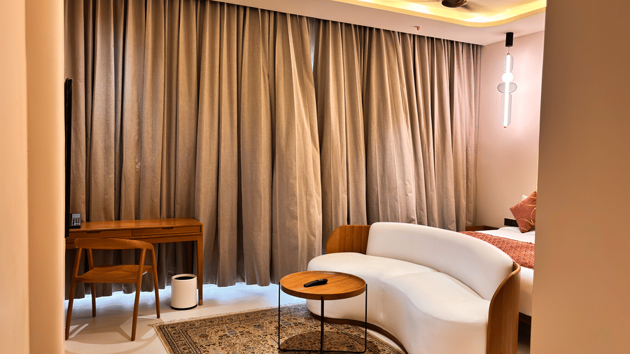 A white sofa and a small round wooden table sit on a patterned rug in a room with floor-to-ceiling curtains at Avanya Resorts N Retreat.