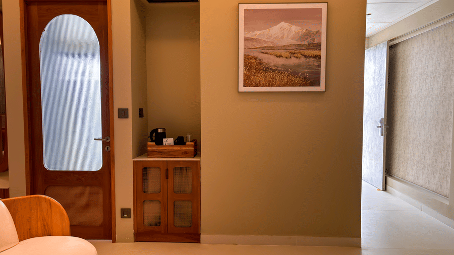 An arched wooden mirror stands next to a recessed coffee station and a framed mountain landscape picture on the wall at Avanya Resorts N Retreat.