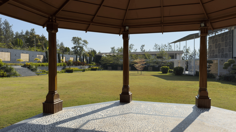 A brightly lit wooden gazebo structure with yellow and orange draping, situated on a green lawn in front of modern, peaked-roof buildings at Bindiga Peak Resorts.