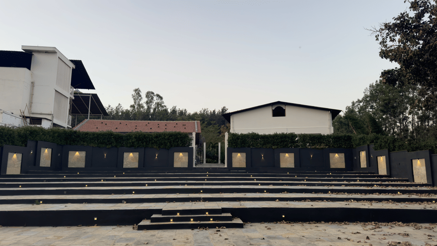 A temporary outdoor seating or viewing area with black risers, set up in a sunlit urban environment, facing a whitewashed wall and residential buildings at Bindiga Peak Resorts.