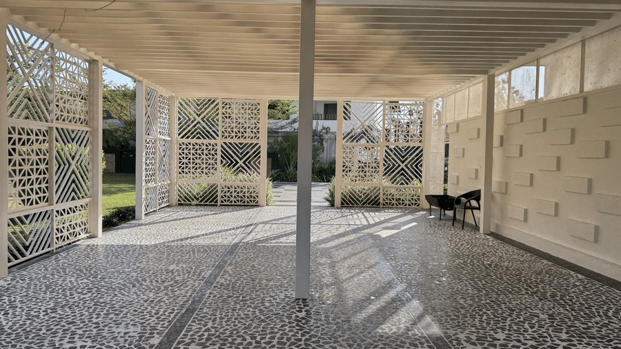 Modern outdoor covered walkway featuring a patterned pebble flooring, a central pillar, and decorative white lattice walls at Bindiga Peak Resorts.