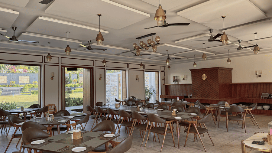 A restaurant dining hall featuring wooden tables, chairs, ceiling fans, and open glass doors leading outside at Bindiga Peak Resort.