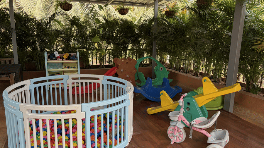 A circular ball pit is placed near a small tricycle, a see saw, potted hedge plants in a play zone at Bougainvillea, Alibaug.