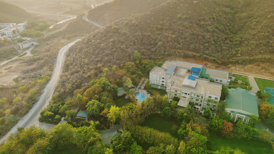 Aerial view of Essentia Luxury Resort & Spa, the best resort in Udaipur for couples, with a small road and trees in view.