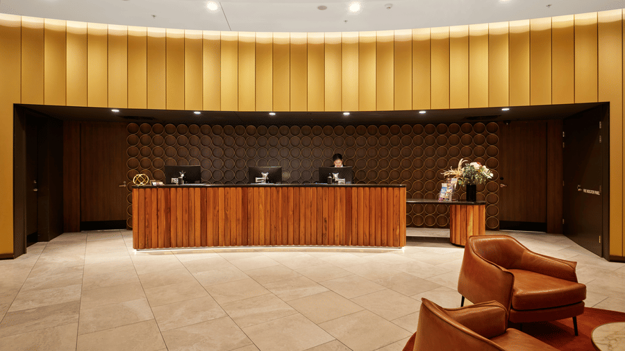A minimalist and grand hotel reception area featuring a long wooden desk and a curved, gold-panelled feature wall.