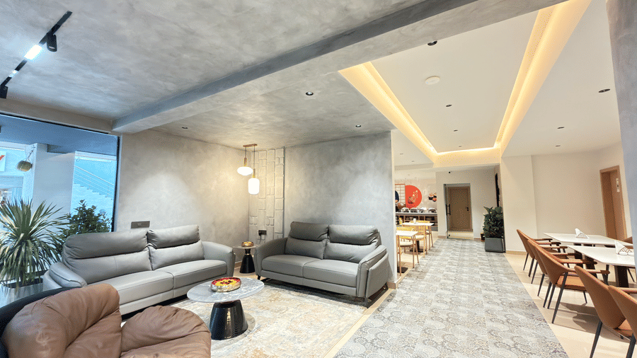 Spacious hotel lobby with contemporary seating, indoor plants, patterned flooring, warm lighting, and an adjoining dining area.