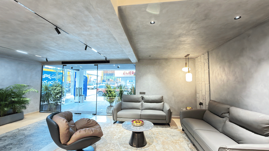 Elegant hotel lounge featuring grey sofas, a statement armchair, round coffee table, indoor plants, and a bright glass entrance.
