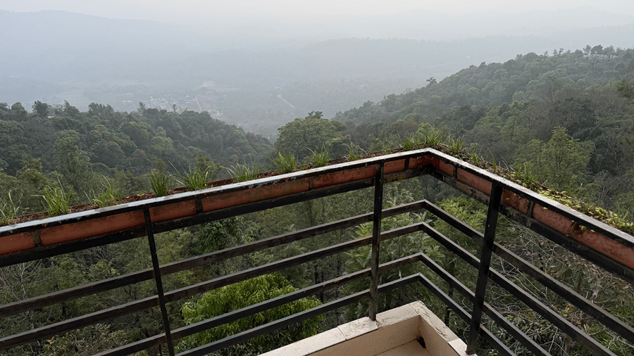 A balcony with a black metal railing overlooking misty green hills and forests | Kollanoor Guest House, Coorg