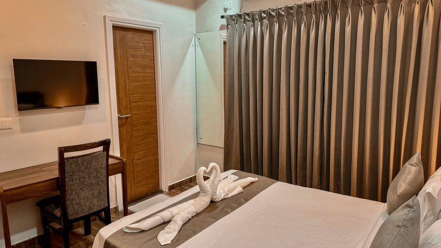 Corner view of the bedroom of Coral 4BHK featuring its queen size bed with folded towels on it, facing a wall-mounted TV | Kove Smart Stays