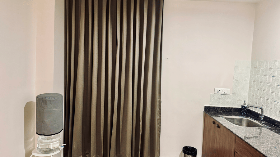 Kitchen of Coral 4BHK at Kove Smart Stays furnished with a separate water facility placed in front of closed curtains, and a countertop on the other side.