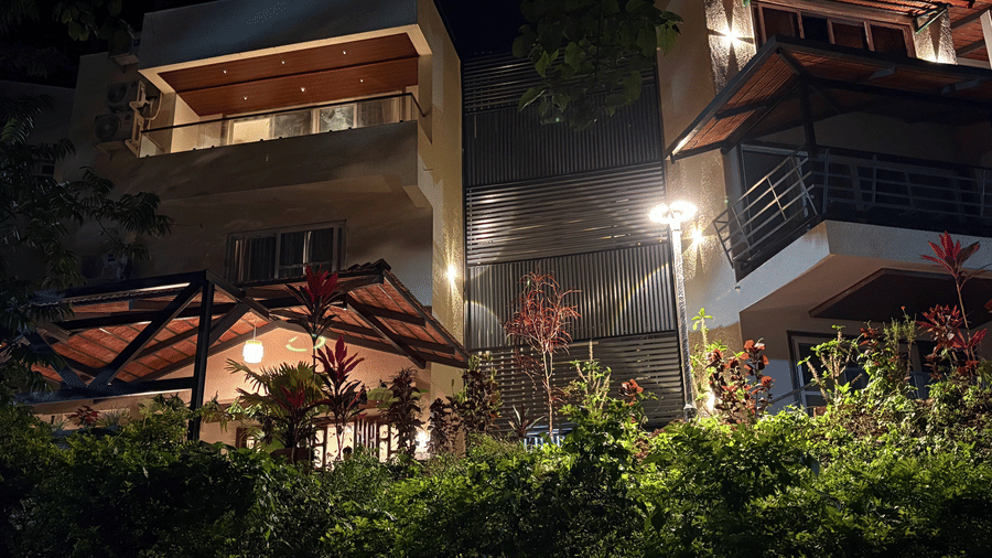 Warmly lit exterior of Lords Riverside Resort, Muduba - Shivamogga at night featuring modern balconies and green landscaping.