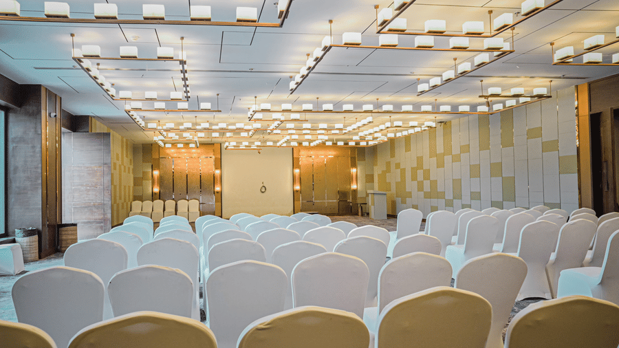 A close-up view of the back rows of chairs in an event space, with a stage and backdrop visible in the distance | Pushkara Resort & Spa, Ajmer