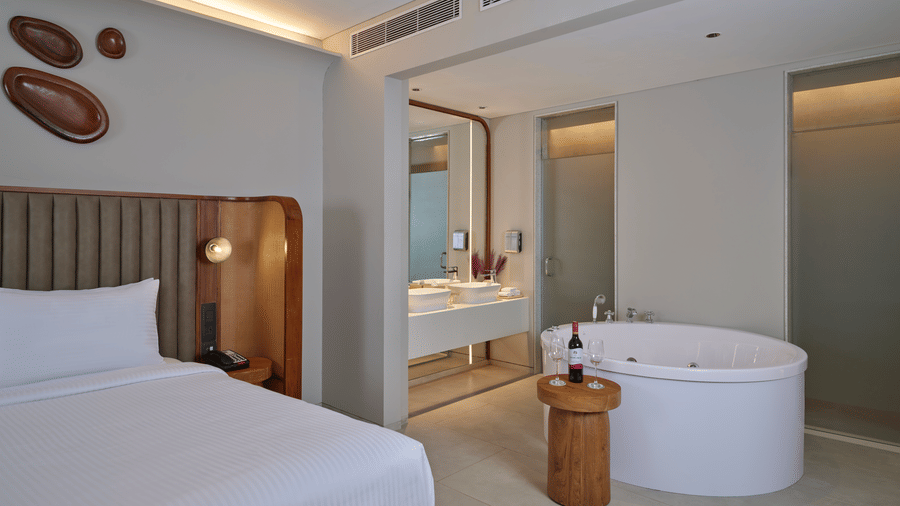 The Intimate Escape Suite at Swosti Premium Beach Resorts, Puri, displaying  a bathtub, toileteries, and bed beside it.