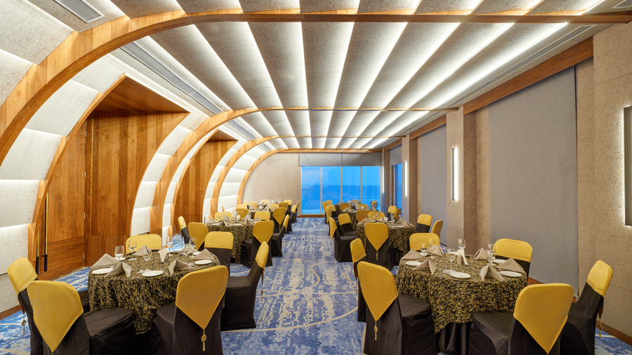 The Portrait hall at Swosti Premium Beach Resorts, Puri, with a unique curved, ribbed ceiling, set up with tables and chairs, facing the window.