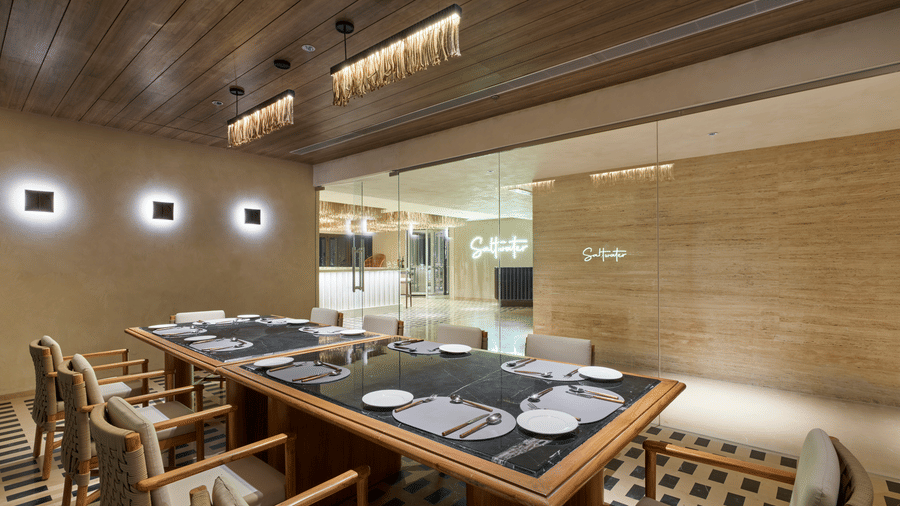 The Saltwater dining at Swosti Premium Beach Resorts, Puri, with wooden tables and chairs, a slatted wood ceiling, and warm lighting.