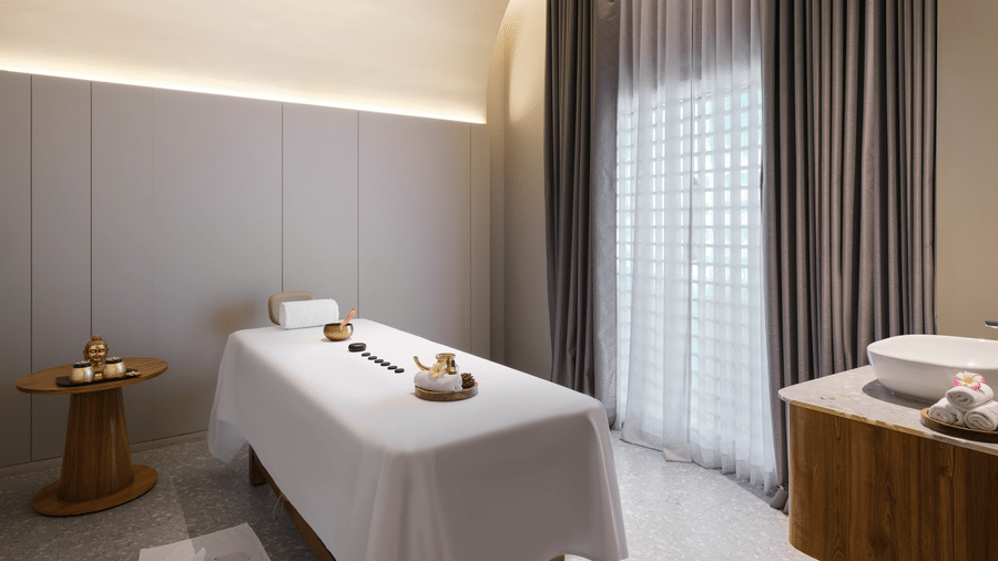 The spa room at Swosti Premium Beach Resorts, Puri, with a massage table, sheer curtains, and wooden furniture.