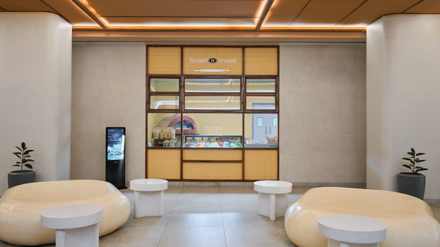 The café  BNC at Swosti Premium Beach Resorts, Puri, featuring large seating, white side tables, a wooden slatted ceiling, and a wooden partition wall with shelves.