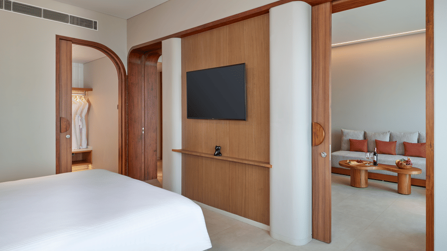 The Oasis Suite bedroom at Swosti Premium Beach Resorts, Puri, with a double bed, wooden accents, and a door revealing a separate area with seating.