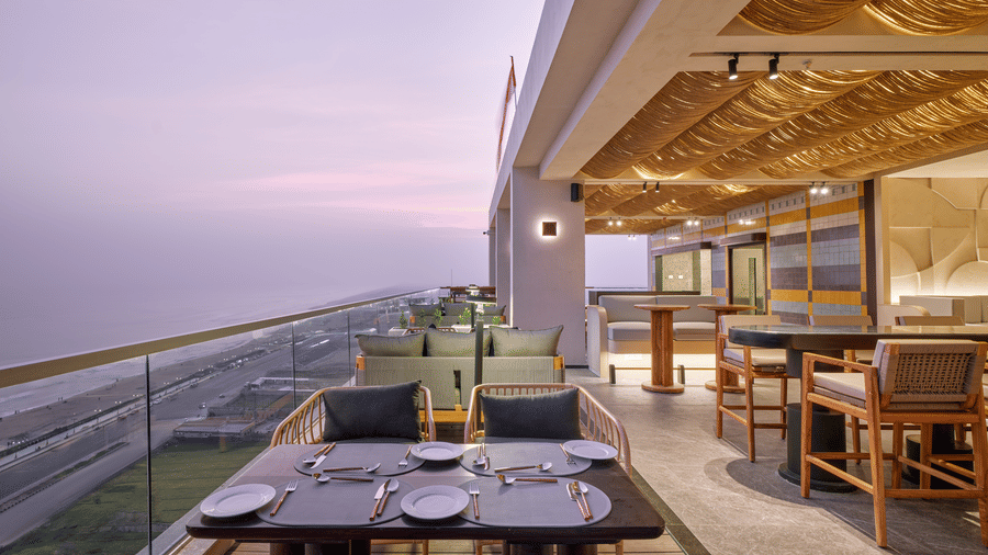 The Saltwater dining at Swosti Premium Beach Resorts, Puri, overlooking the ocean at dusk, with tables set and a glass railing.