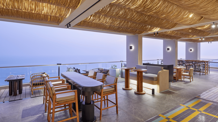 The Saltwater dining at Swosti Premium Beach Resorts, Puri, with a thatched roof, wooden furniture, and views of the sea.