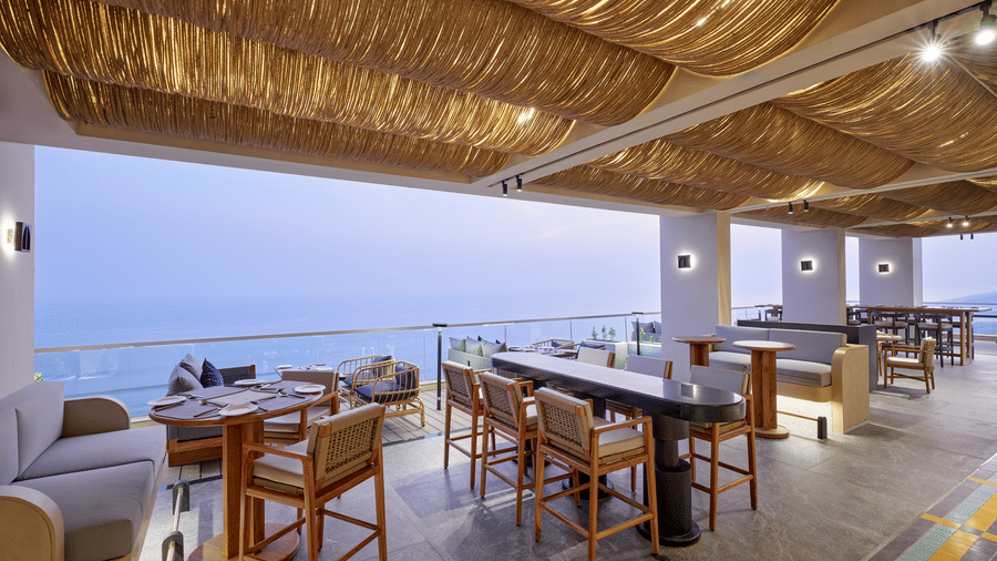 The Saltwater dining at Swosti Premium Beach Resorts, Puri, showing various seating arrangements under a thatched canopy with an sea backdrop.