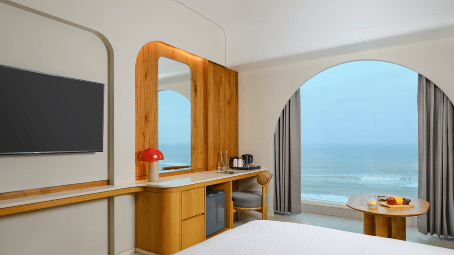 The Sea View Room (Front View) at Swosti Premium Beach Resorts, Puri, with a large window offering a magnificent view of the sea, a desk, and a large television.
