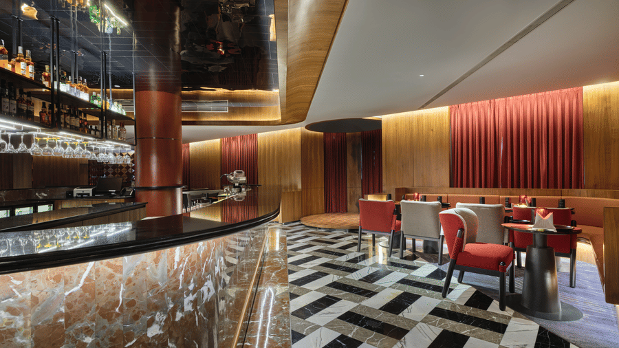 The well-lit bar of Swosti Premium, Bhubaneswar, with chairs, tables, a long slab, and glasses and bottles arranged in a stand.