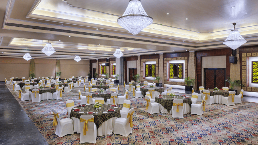 The well-lit Chanakya Banquet at Swosti Premium, Bhubaneswar, featuring chairs, tablets, chandeliers, and windows.