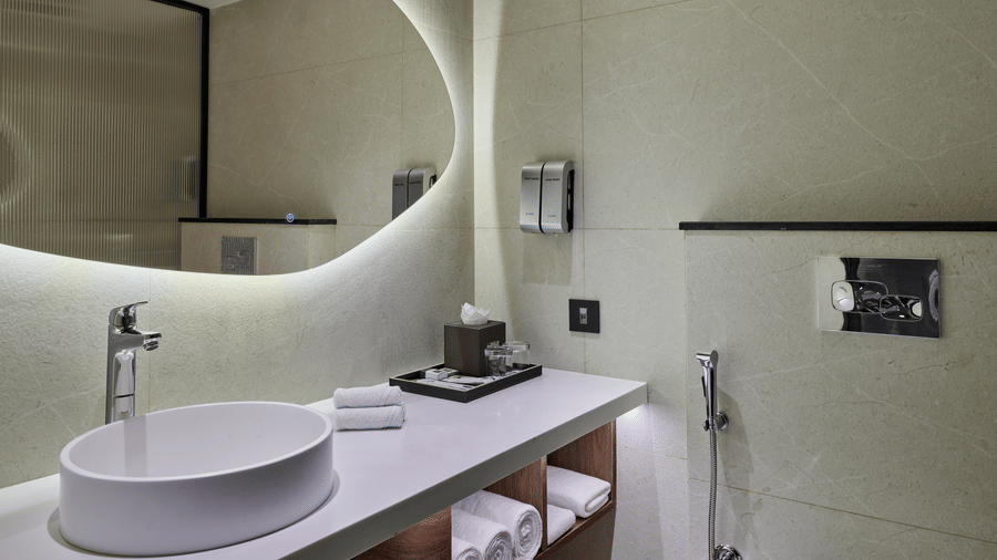 The Elite Room bathroom at Swosti Premium, Bhubaneswar, featuring a sink, toileteries, and a mirror.