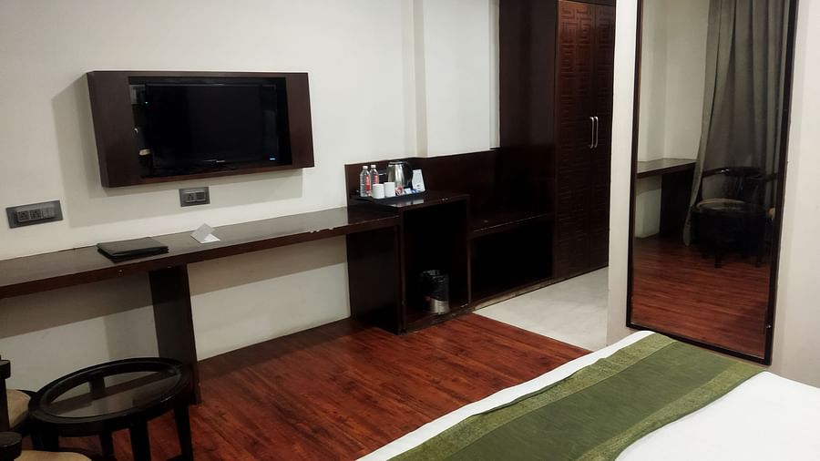 A sleek hotel room with a large mirror, a dark wood desk and a bed with a green accent runner - TGI Apple Inn, Jaipur 