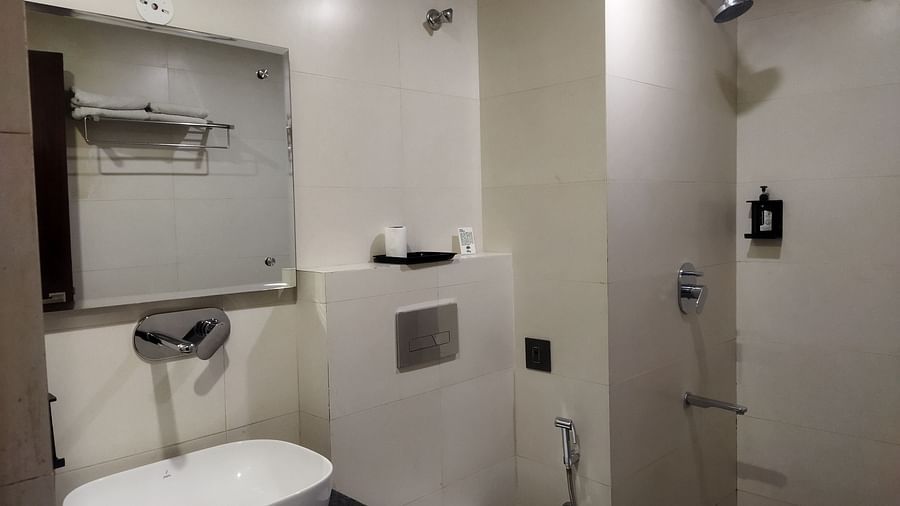 A hotel bathroom with modern fixtures, a wall-mounted sink, a glass shower and beige tiles - TGI Apple Inn, Jaipur 