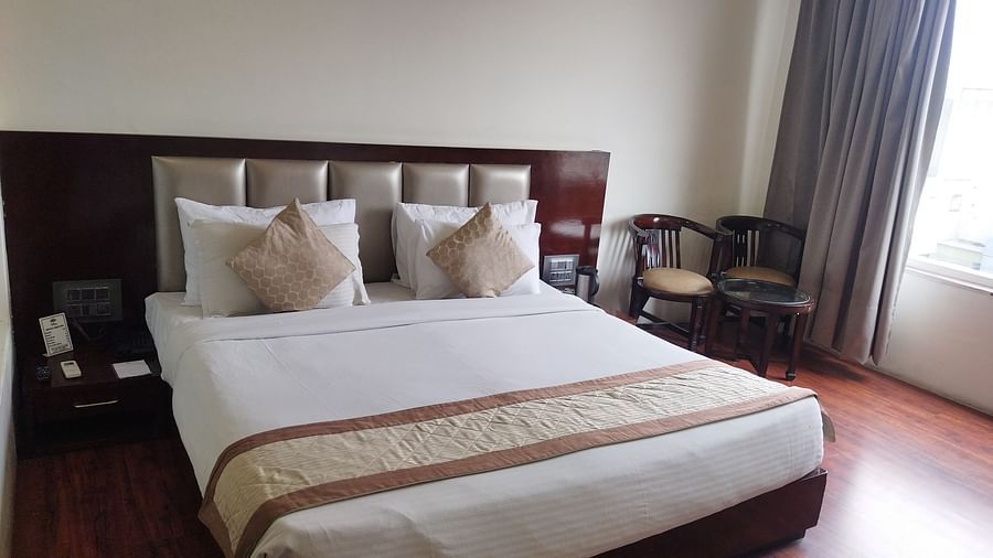 A hotel room with a large bed draped in beige and brown linens and furniture to relax - TGI Apple Inn, Jaipur 