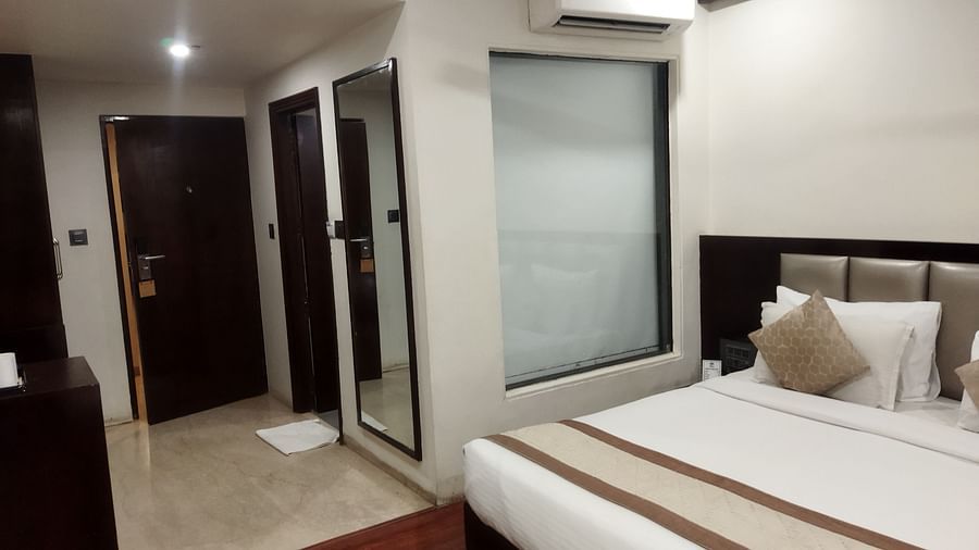 A spacious hotel room with a large window, a queen sized bed and a reflective wardrobe - TGI Apple Inn, Jaipur 