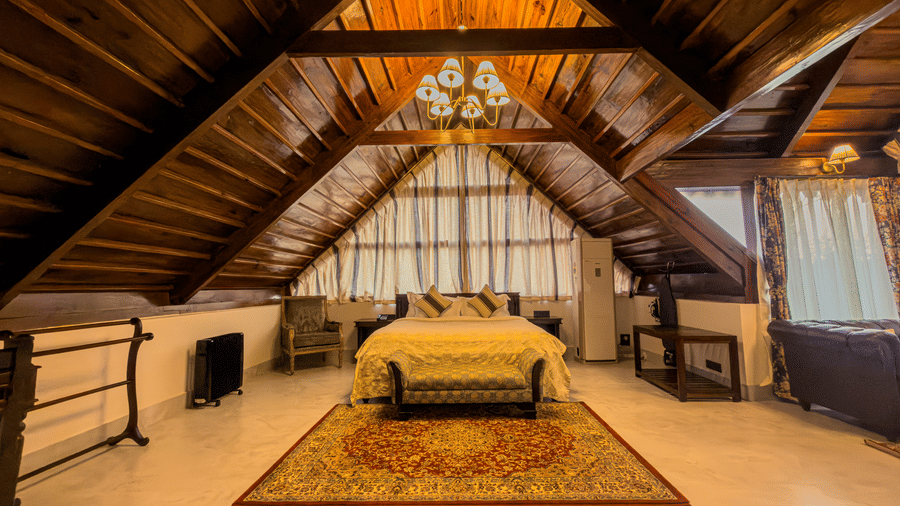 The Tagore Suite at The Heritage Club Tripura Castle Hotel and Spa, Shillong, featuring a grand bed placed under a steep wooden ceiling with a classic chandelier.