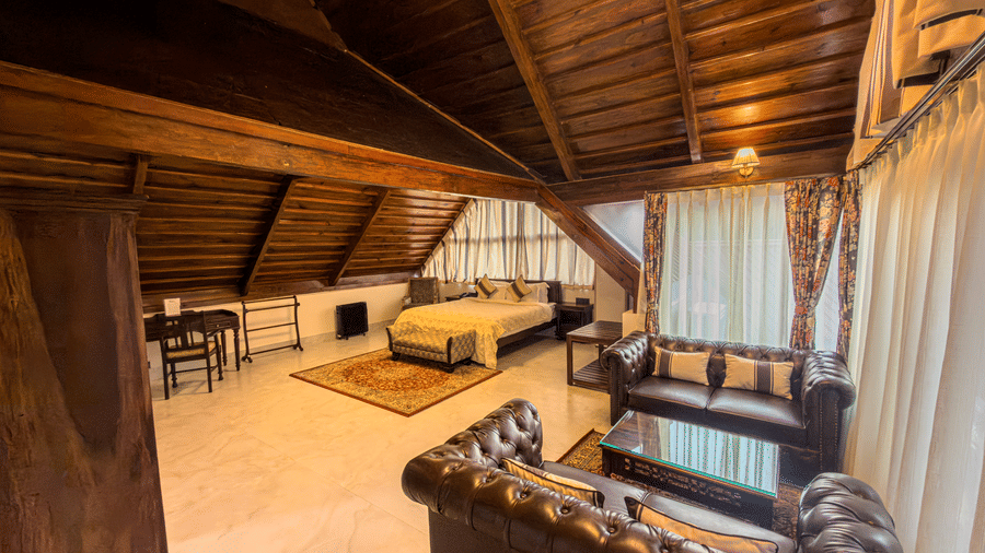 The Tagore Suite at The Heritage Club Tripura Castle Hotel and Spa, Shillong, featuring a bedroom with a wooden sloped ceiling and a plush seating area.