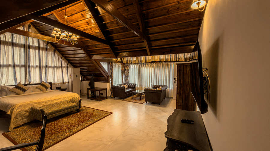The Tagore Suite at The Heritage Club Tripura Castle Hotel and Spa, Shillong, featuring the seating area and large windows under rustic wooden beams.