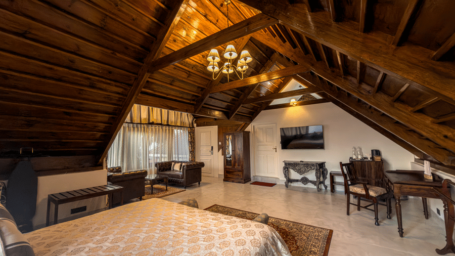 The Tagore Suite at The Heritage Club Tripura Castle Hotel and Spa, Shillong, features a large bed and a wall mounted television under a rustic roof.