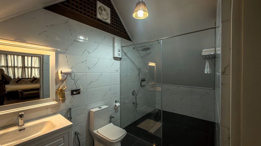 Bathroom of the Tagore Suite at The Heritage Club Tripura Castle Hotel and Spa, Shillong, featuring a western toilet, a vanity, and a walk-in shower area.