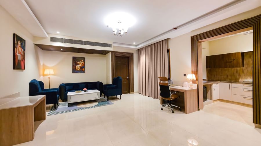 A wide angle shot of the expansive living area featuring a work station in the corner along with a blue coloured couch set in the Empress Suite at The Meriton.