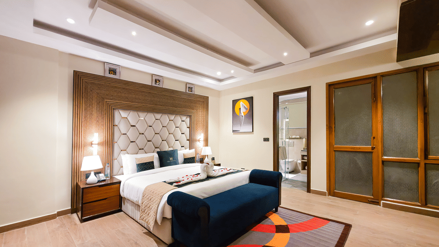 A wide angle shot of the bedroom at the Empress Suite featuring a plush double bed along with a rug on the floor in front of it at The Meriton.
